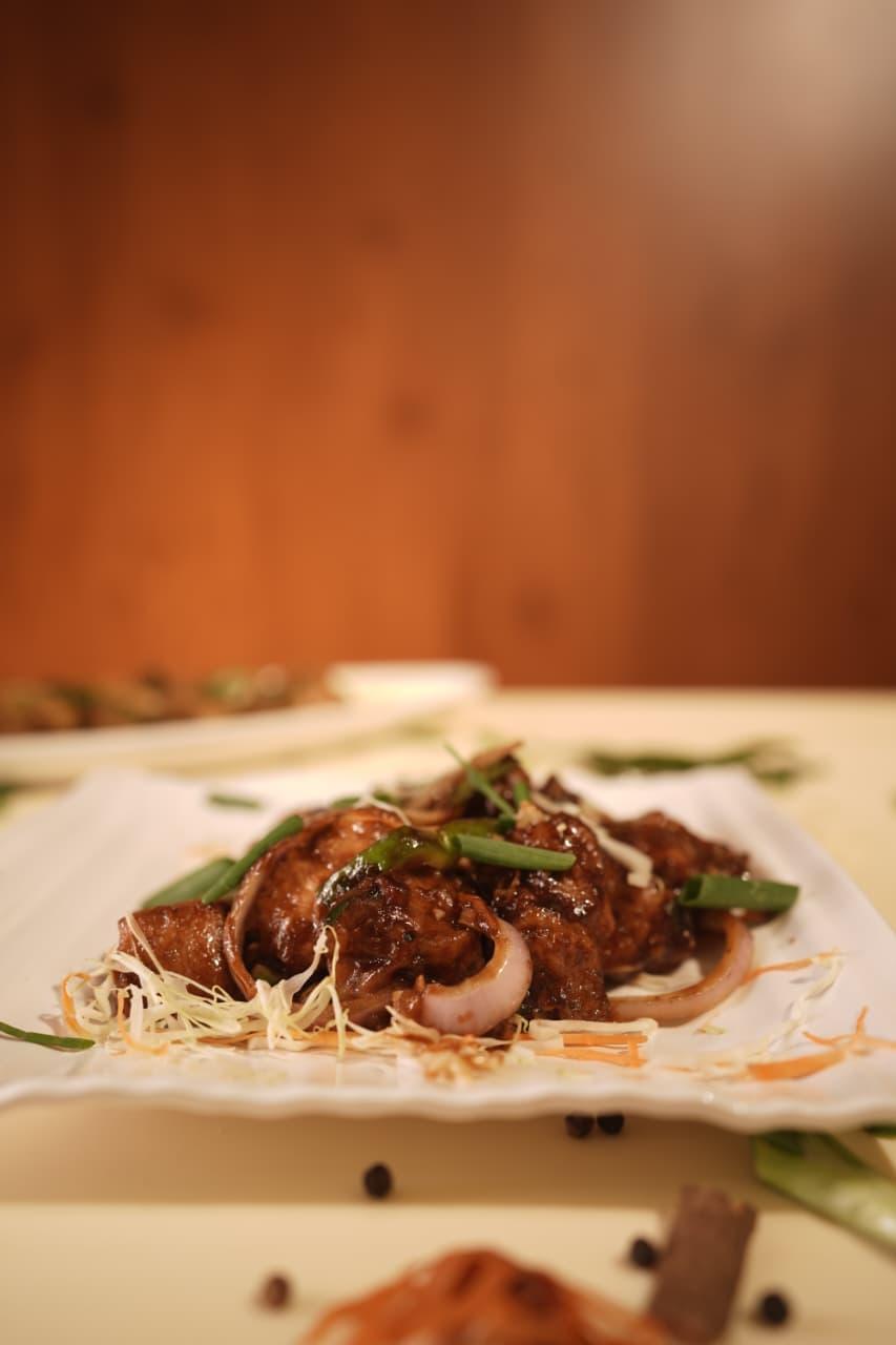 Chilli chicken with onion and spring onion on a white plate
