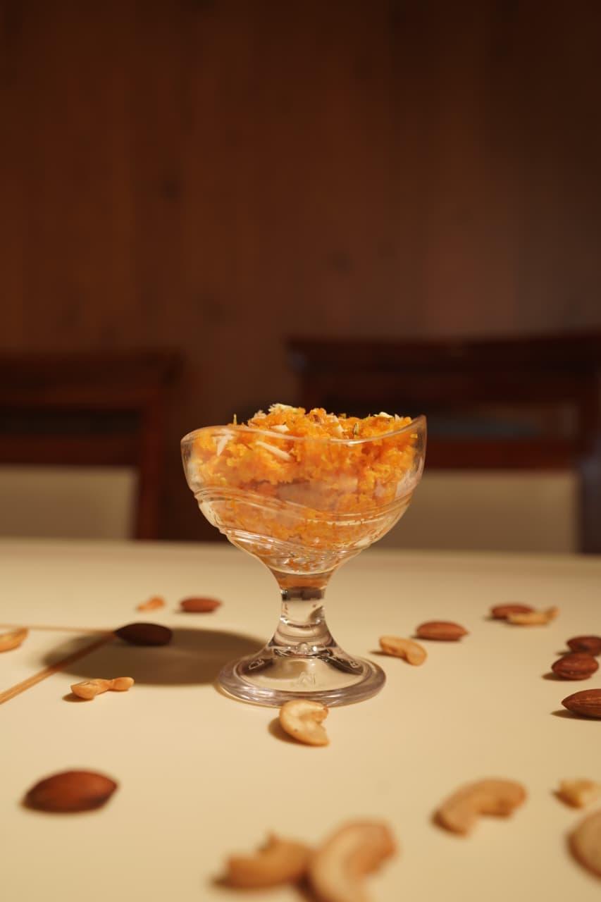 Gajar halwa in a footed glass bowl surrounded by almonds and cashews