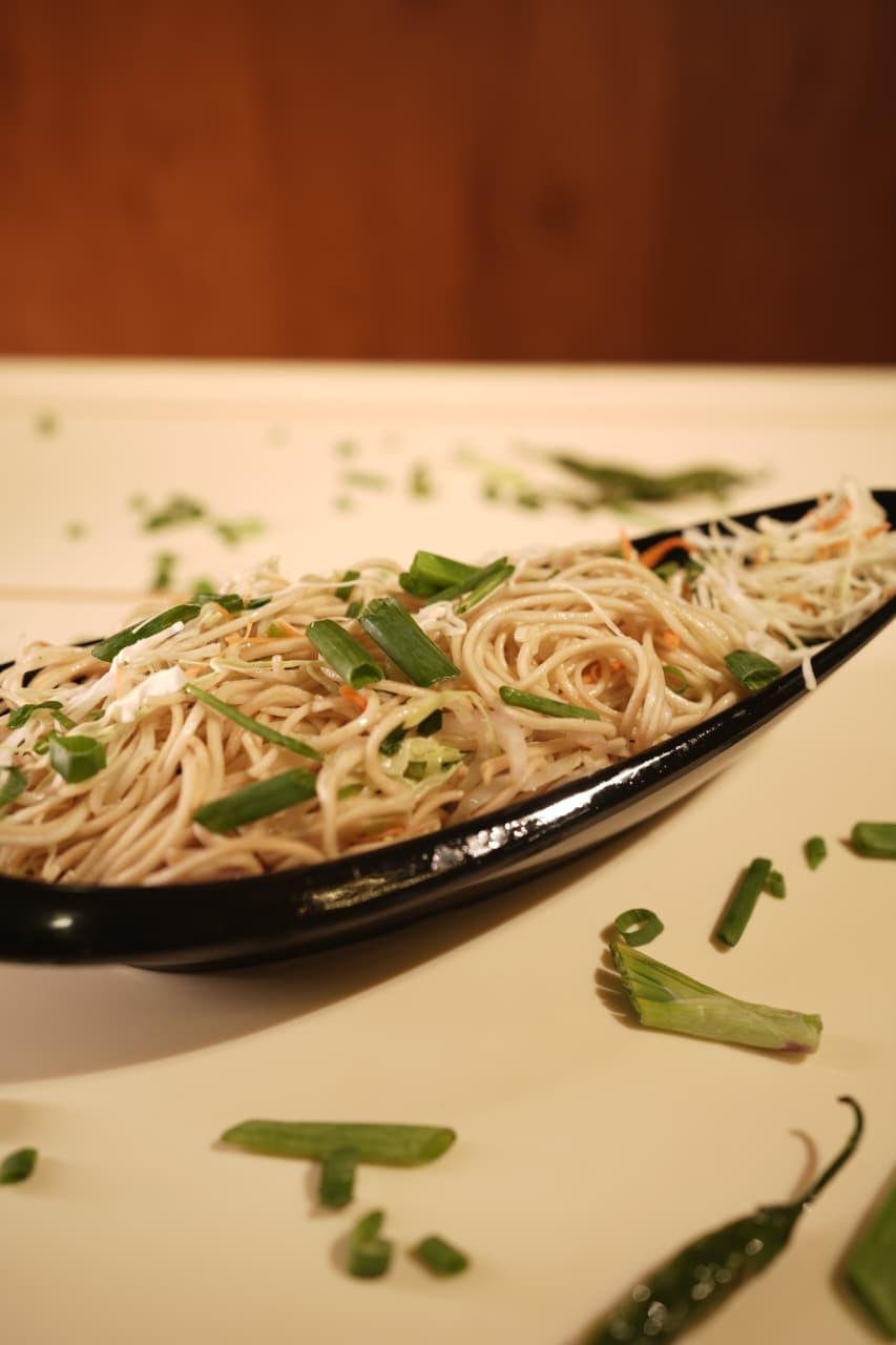 Hakka noodles with spring onion in a black boat-shaped dish