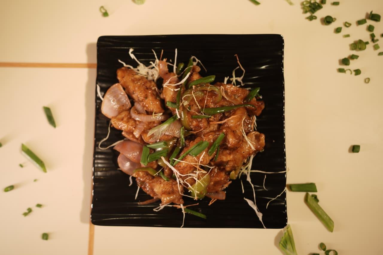 Dragon chicken with peppers and onion on a black plate, seen from above