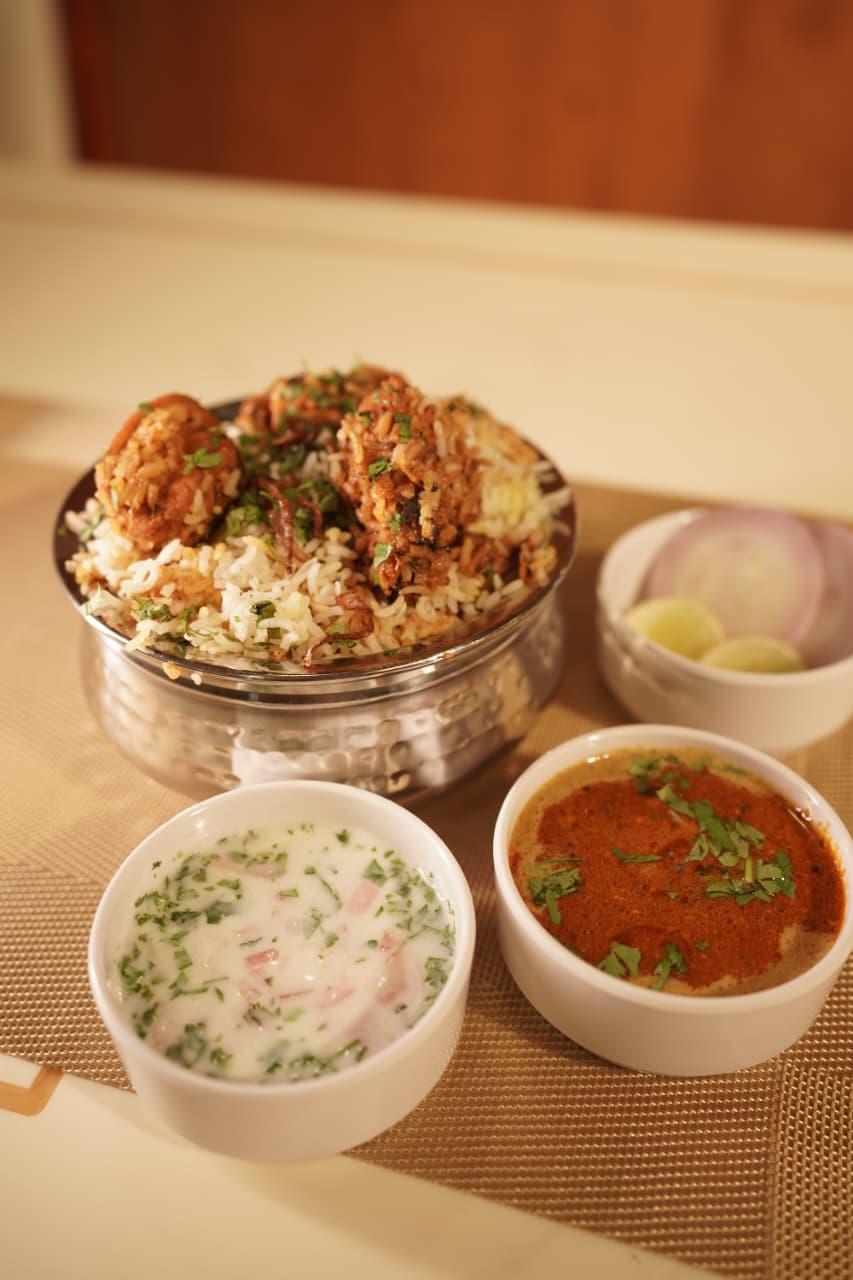 Biryani in a steel handi with raita and salan on the side